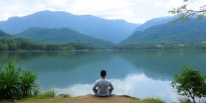 Person meditating by a serene lake in nature.